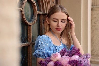 Photo of Beautiful woman with bouquet of spring flowers near building outdoors