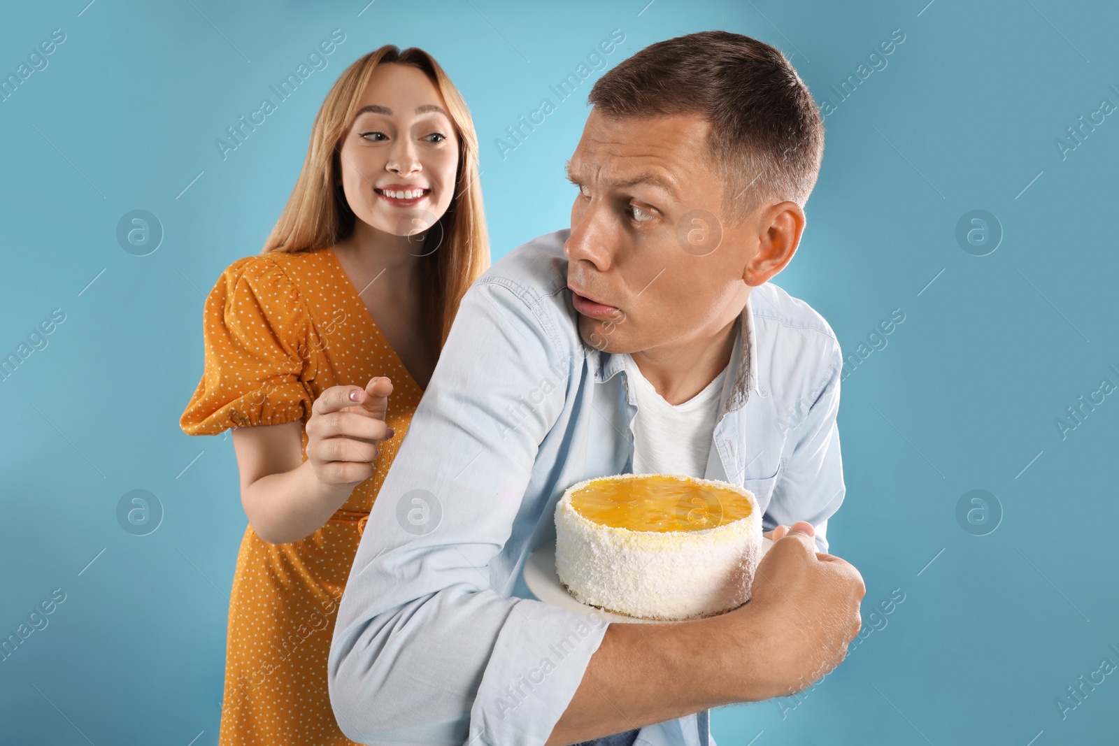 Photo of Greedy man hiding tasty cake from woman on turquoise background