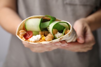 Photo of Woman holding delicious hummus wrap with vegetables, closeup