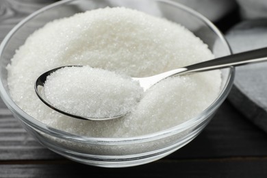 Photo of Granulated sugar in bowl and spoon on black wooden table, closeup