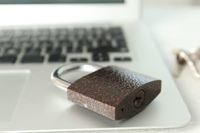 Photo of Metal lock and laptop on table, closeup. Protection from cyber attack
