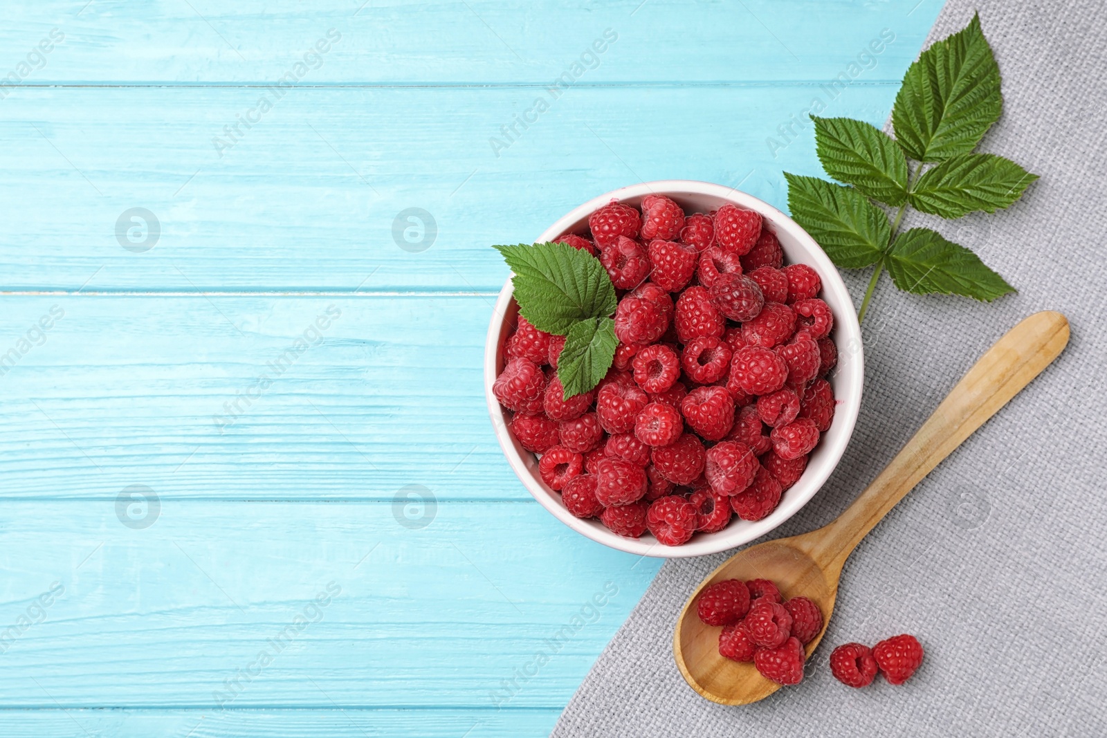 Photo of Bowl and spoon with ripe aromatic raspberries on wooden table, top view