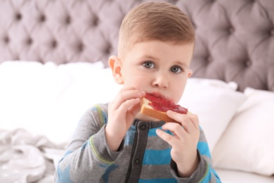 Cute little boy eating toast with sweet jam at home