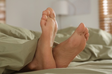 Photo of Person in bed with green linens at home, closeup on feet