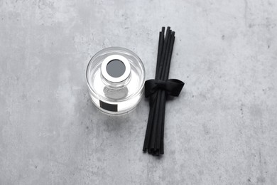 Photo of Reed sticks near glass bottle with aromatic liquid on gray marble table, flat lay