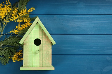 Beautiful bird house and mimosa flowers on blue wooden table, flat lay. Space for text