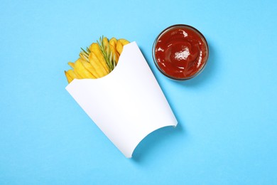 Photo of Paper cup with French fries, rosemary and ketchup on light blue table, flat lay