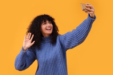 Photo of Beautiful young woman taking selfie with smartphone on orange background