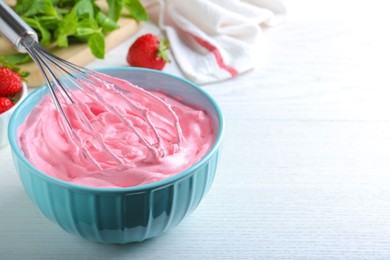 Photo of Whipping strawberry cream with balloon whisk on white wooden table, closeup. Space for text