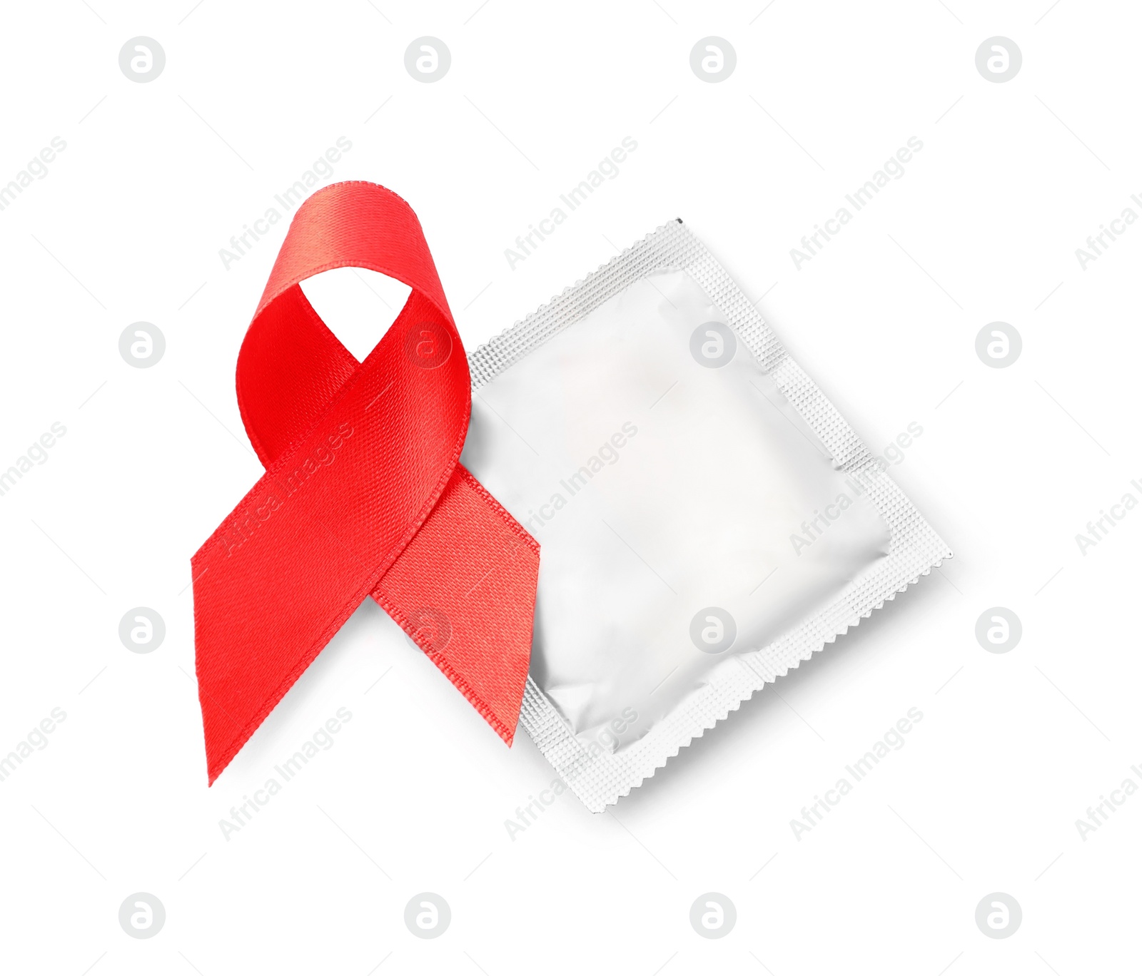 Photo of Red ribbon and condom isolated on white, top view. AIDS disease awareness