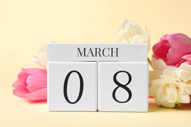 Photo of International Women's day - 8th of March. Wooden block calendar and beautiful flowers on beige background