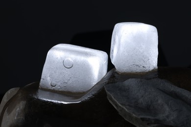 Crystal clear ice cubes on stone against dark background, closeup