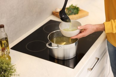 Man pouring delicious soup into bowl in kitchen, closeup