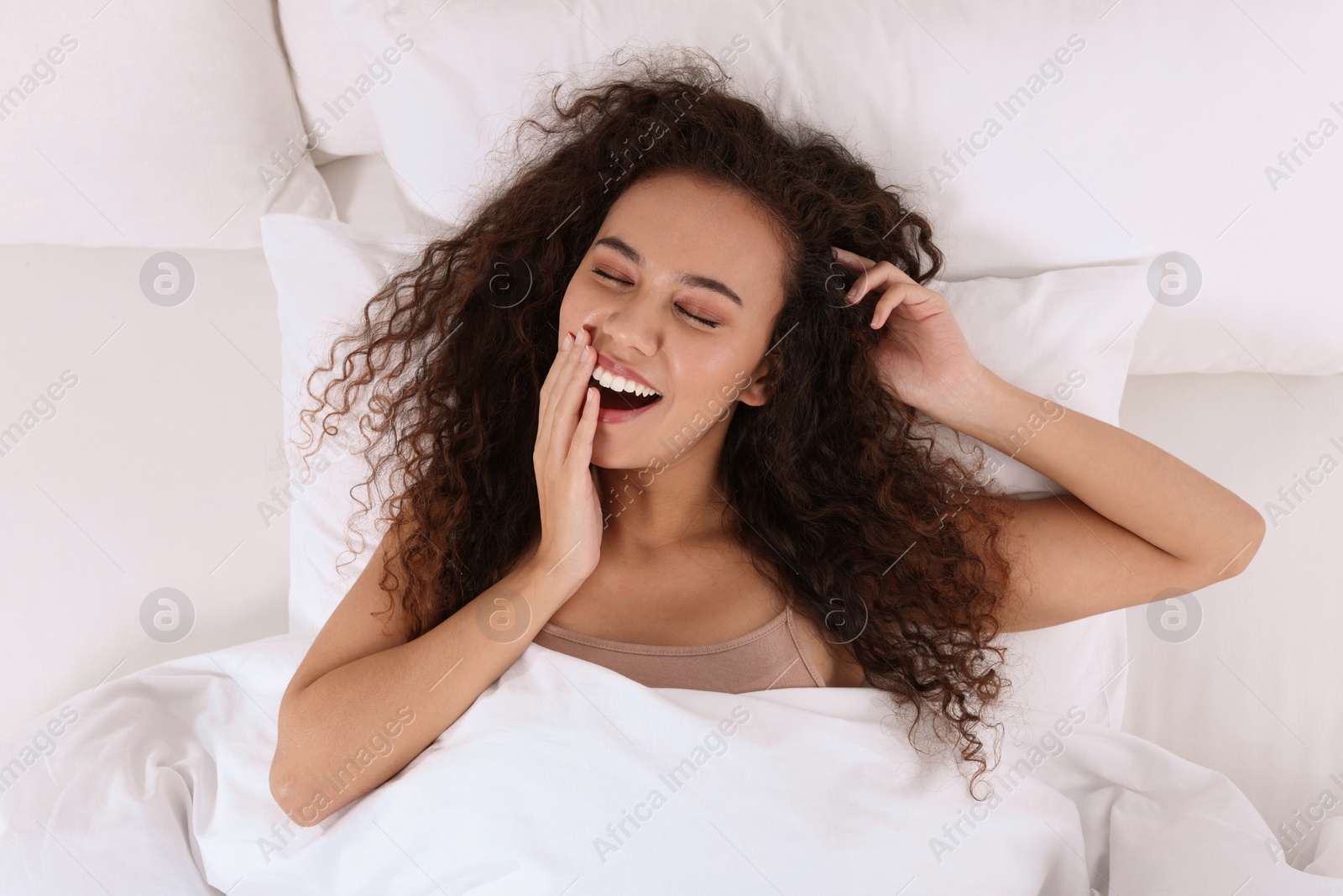 Photo of Happy African American woman awakening in bed, top view