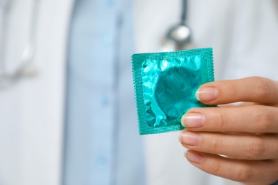 Female doctor holding condom, closeup. Safe sex concept