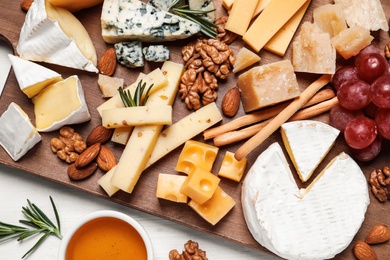 Photo of Cheese plate with honey, grapes and nuts on white table, top view