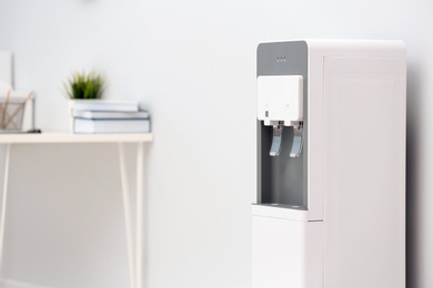 Photo of Modern water cooler near light wall in office