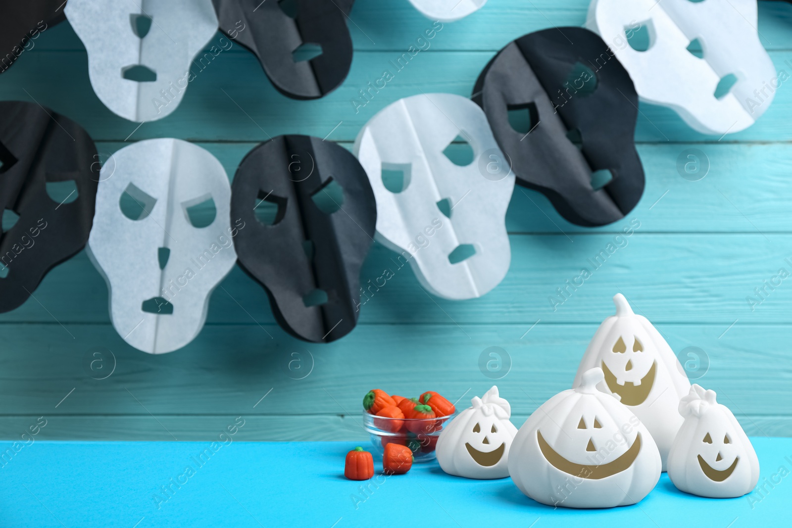 Photo of Jack-o-Lantern holders and candies on light blue table against decorated wooden background. Halloween decor