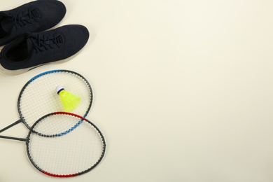 Photo of Rackets, sneakers and shuttlecock on beige background, flat lay with space for text. Badminton equipment