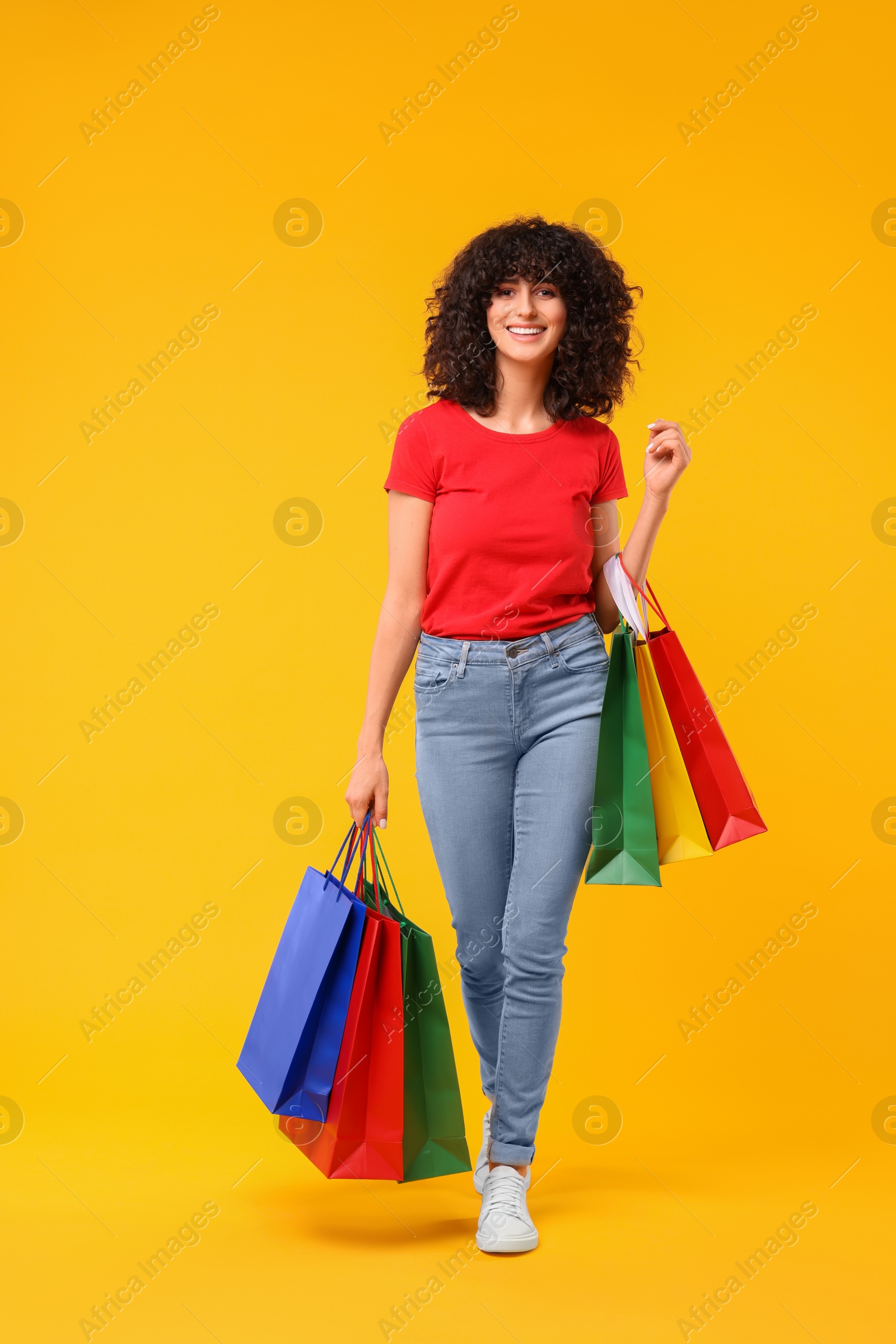 Photo of Happy young woman with shopping bags on yellow background