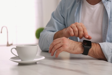 Young man using smart watch at table in kitchen, closeup