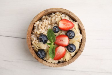 Photo of Tasty oatmeal with strawberries, blueberries and almond petals in bowl on white wooden table, top view