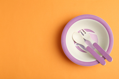 Photo of Small bowl, fork and spoon on orange background, top view with space for text. Serving baby food