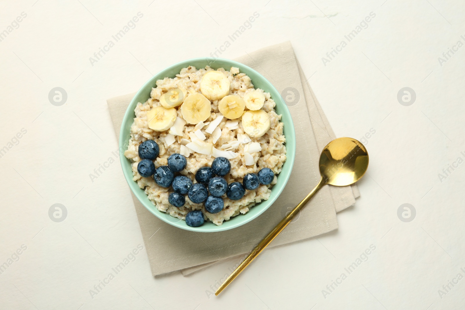 Photo of Tasty oatmeal with banana, blueberries, coconut flakes and honey served in bowl on beige table, top view