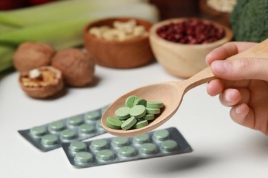 Photo of Woman holding spoon of pills at table with foodstuff, closeup. Prebiotic supplements