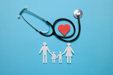 Photo of Paper family figures, red heart and stethoscope on light blue background, flat lay. Insurance concept