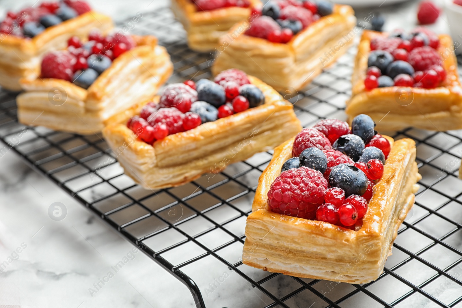 Photo of Cooling rack and fresh delicious puff pastry with sweet berries on white marble table