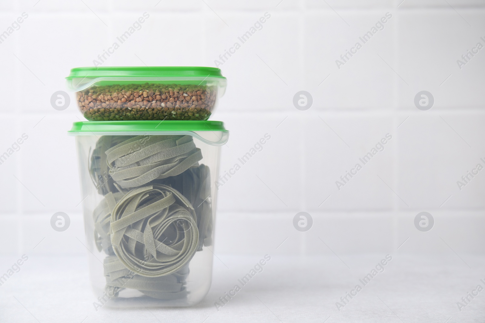 Photo of Plastic containers filled with food products on white table near tiled wall. Space for text