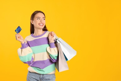 Photo of Happy young woman with shopping bags and credit card on yellow background, space for text. Big sale