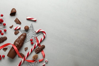 Photo of Flat lay composition with chocolate Santa Claus candies and Christmas decorations on light grey table. Space for text