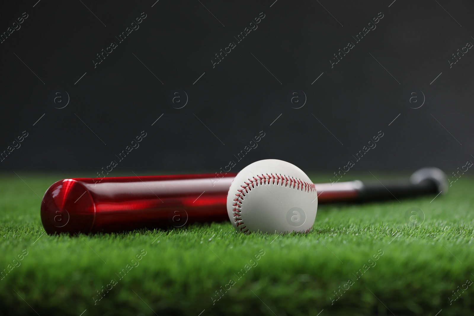 Photo of Baseball bat and ball on green grass against dark background. Space for text