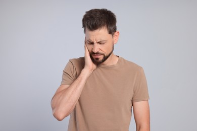 Man suffering from ear pain on grey background