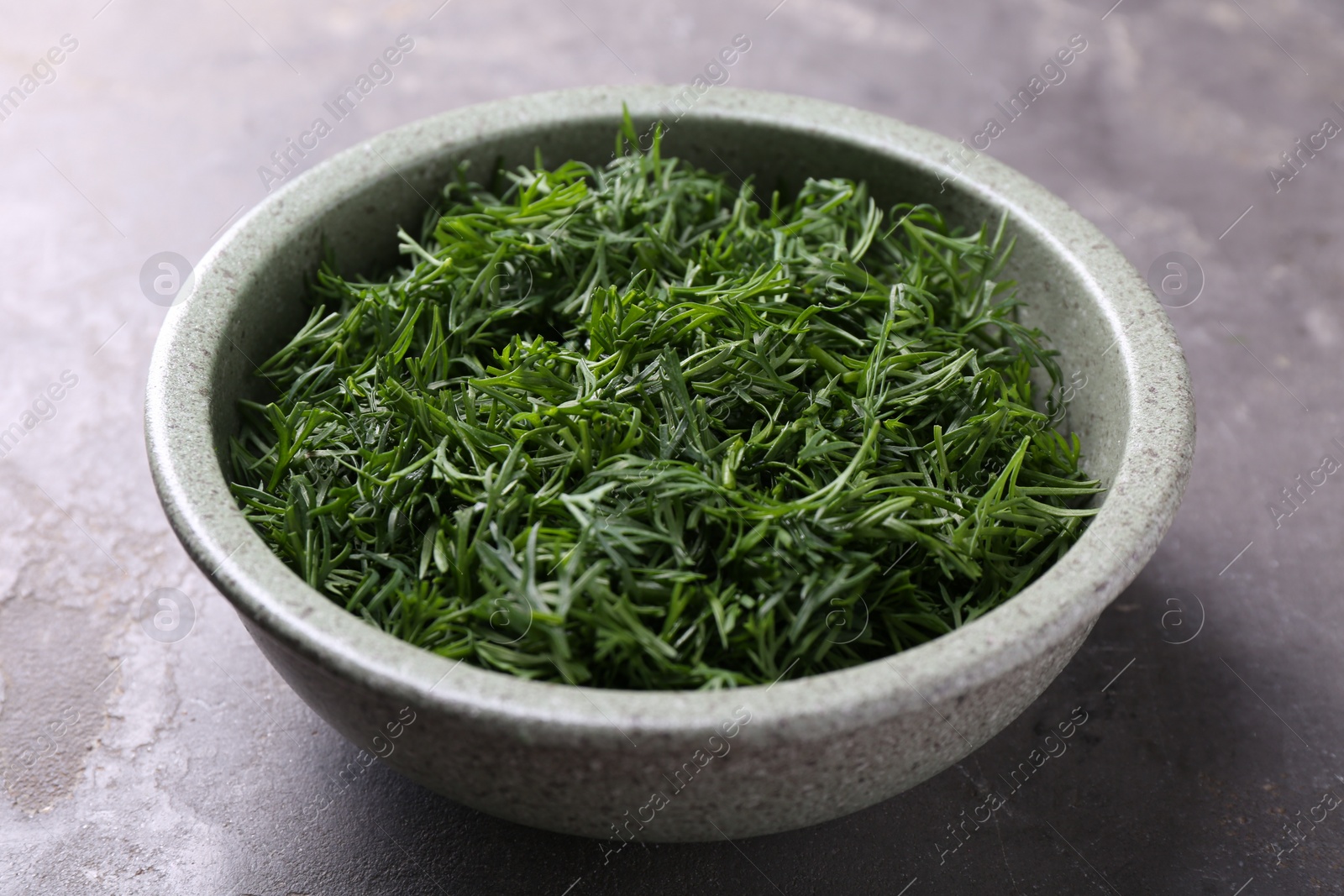 Photo of Fresh cut dill in bowl on grey textured table, closeup