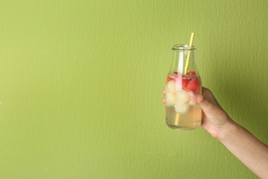 Photo of Woman holding glass bottle of melon and watermelon ball cocktail against light green background. Space for text