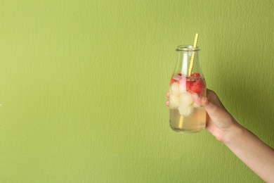 Woman holding glass bottle of melon and watermelon ball cocktail against light green background. Space for text