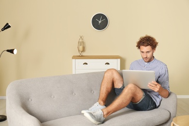 Photo of Young man with laptop sitting on sofa at home