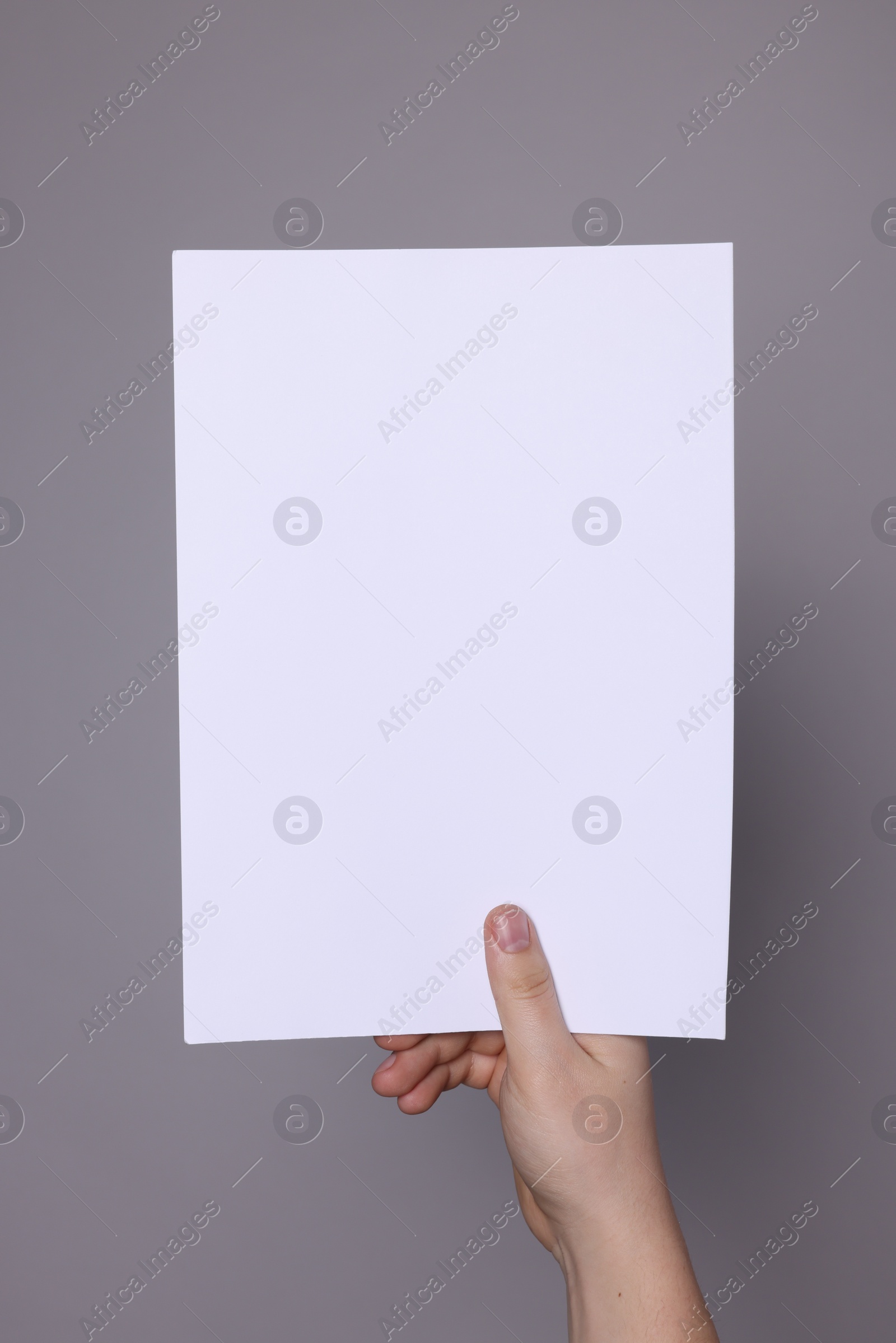 Photo of Woman holding sheet of paper on grey background, closeup. Mockup for design