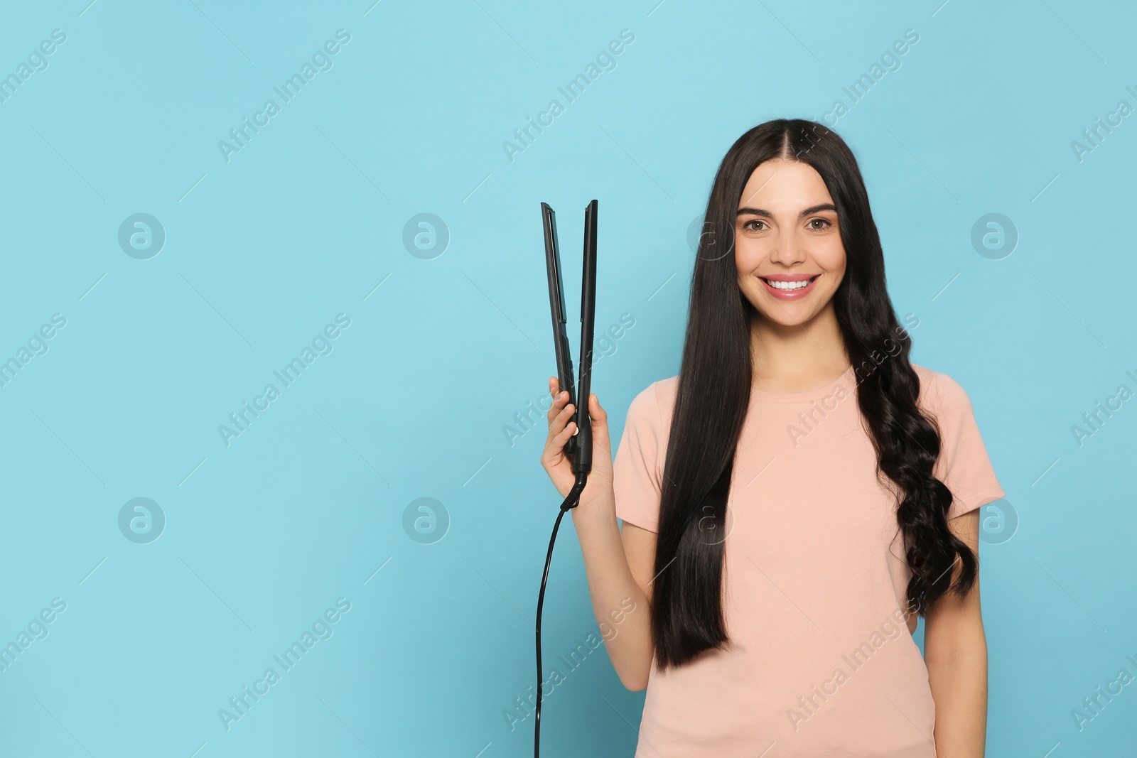 Photo of Beautiful happy woman with hair iron on light blue background. Space for text