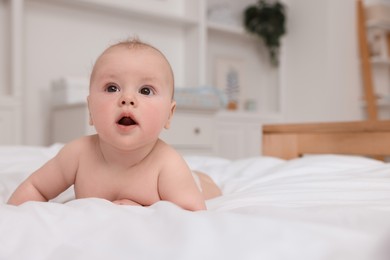 Photo of Cute baby lying on white bed at home, space for text