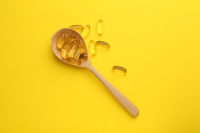 Photo of Vitamin capsules in wooden spoon on yellow background, top view