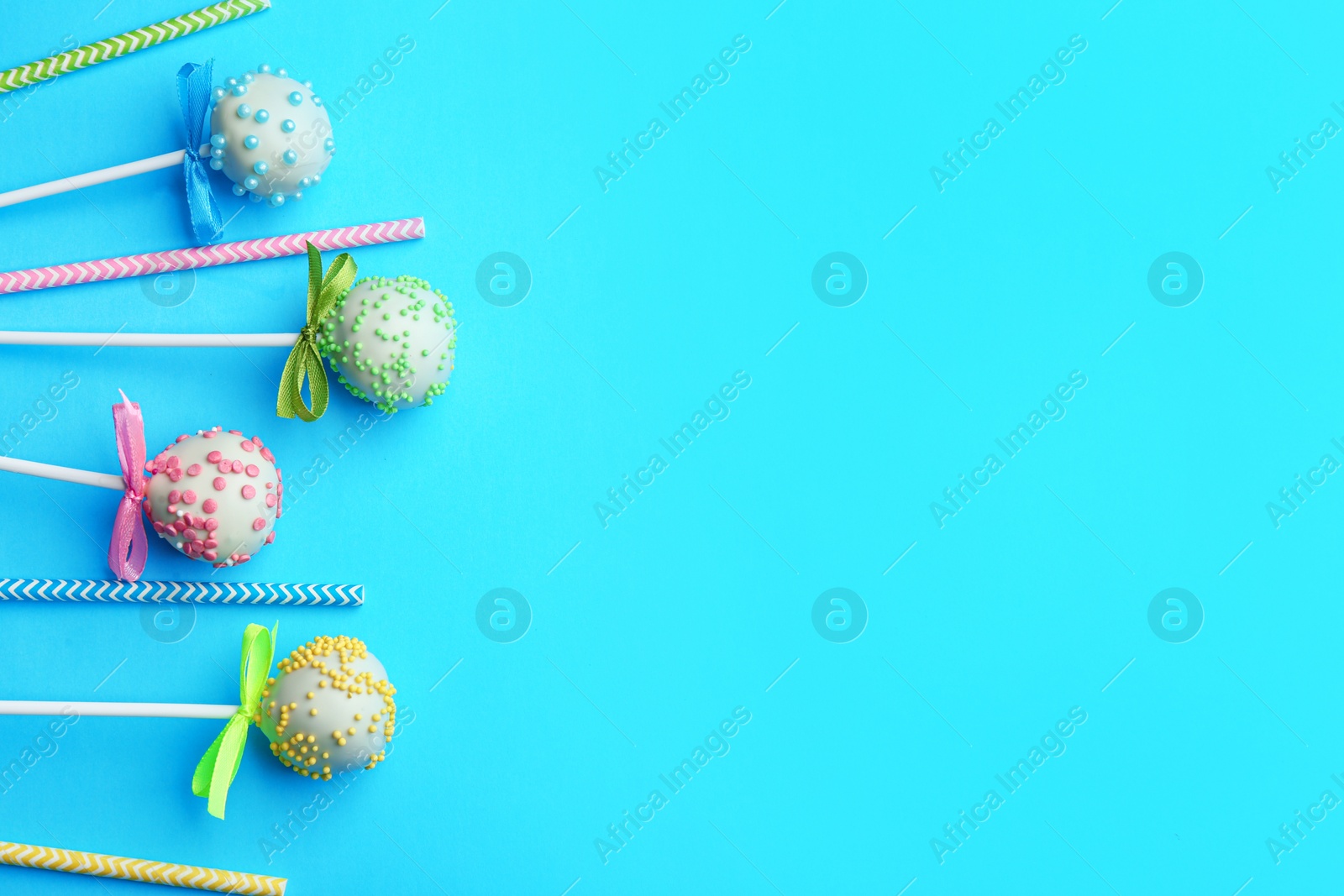 Photo of Tasty cake pops and straws on light blue background, flat lay. Space for text