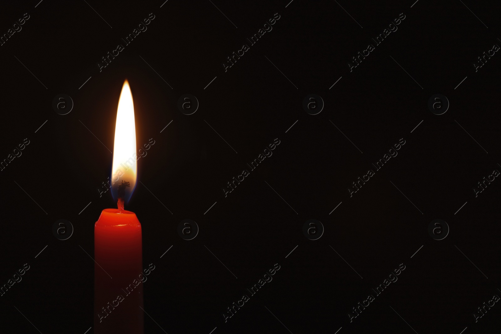 Photo of Wax candle burning on black background, closeup