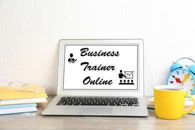 Image of Modern laptop with text BUSINESS TRAINER ONLINE on table indoors