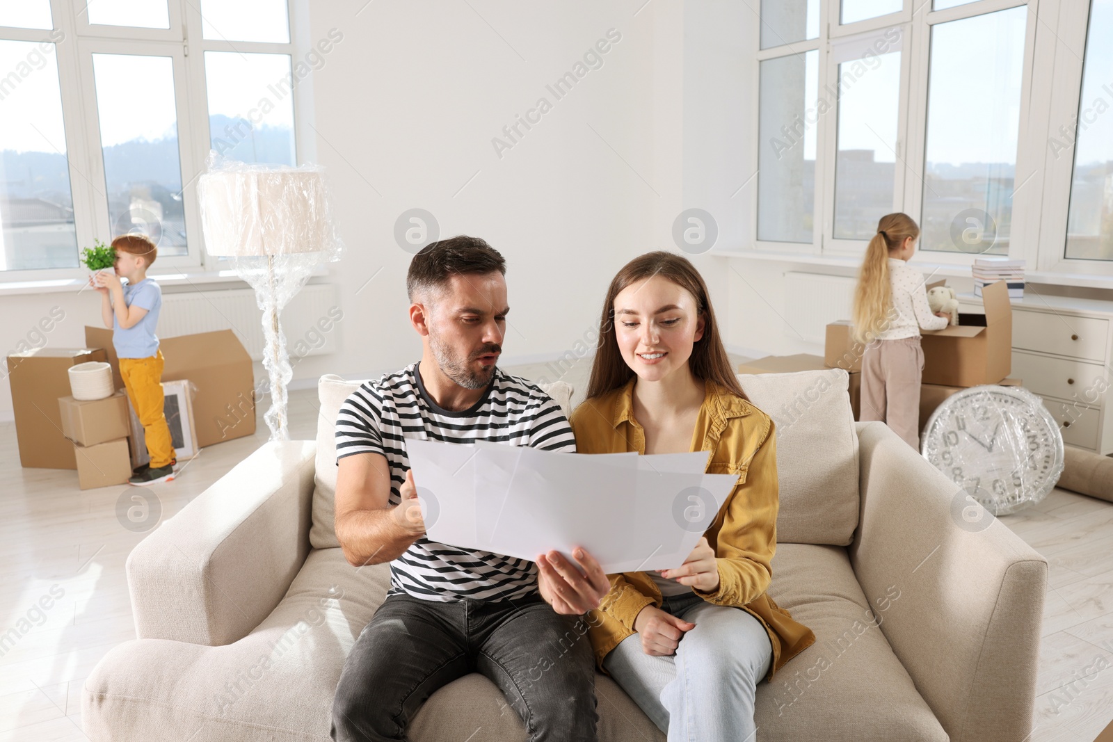 Photo of Family settling into home. Happy wife with husband choosing interior details while daughter and son unpacking boxes in new apartment. Moving day