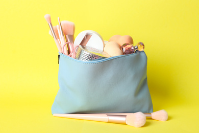 Cosmetic bag with makeup products and beauty accessories on yellow background