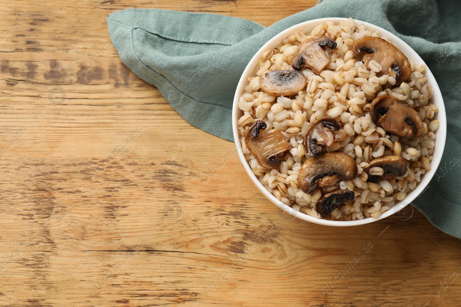 Photo of Delicious pearl barley with mushrooms in bowl on wooden table, top view. Space for text